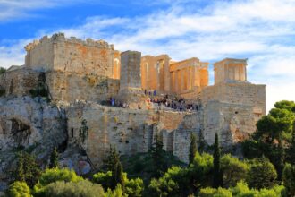 Τουρίστες περπατούν σε αρχαιολογικό χώρο με θέα την Αθήνα, ηλιόλουστη ημέρα, χωρίς διακριτά πρόσωπα