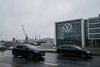 Το λογότυπο της Volkswagen σε κτίριο κεντρικών γραφείων στο Wolfsburg με φόντο συννεφιασμένο ουρανό.