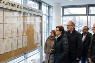 Πολίτες διαβάζουν ανακοινώσεις σε πίνακα μέσα σε γραφείο εύρεσης εργασίας στη Γερμανία