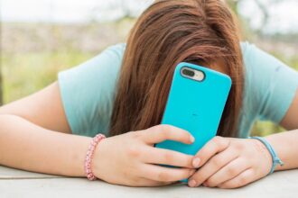 Έφηβη κρατά ένα smartphone στα χέρια της ενώ κάθεται σε δωμάτιο