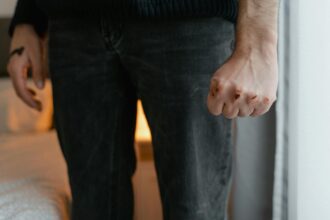 Σιλουέτα γυναίκας σε σκοτεινό δωμάτιο που κοιτάζει έξω από το παράθυρο, συμβολίζοντας την αθέατη ενδοοικογενειακή βία και τη σιωπή των θυμάτων στη Γερμανία