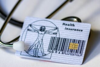 Γραφική απεικόνιση γερμανικής κάρτας υγείας πάνω σε οικονομικά έγγραφα και ευρώ με φόντο θολωμένο κτήριο θεσμικού φορέα