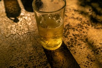 Γραμμή παραγωγής σε γερμανική ζυθοποιία με γυάλινα μπουκάλια μπύρας να μεταφέρονται στον ιμάντα εμφιάλωσης υπό χαμηλό φωτισμό.