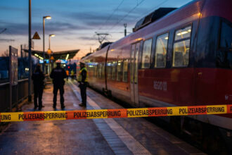 Ένα περιφερειακό τρένο της Deutsche Bahn σταματημένο σε σταθμό της Γερμανίας, με αστυνομική κορδέλα να αποκλείει την αποβάθρα, υπό το φως του δειλινού.