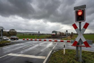 Κόκκινος προειδοποιητικός σηματοδότης και κατεβασμένες μπάρες ασφαλείας σε σιδηροδρομική διάβαση στη Γερμανία
