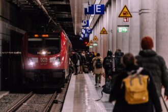 Γενικό πλάνο από σιδηροδρομικό σταθμό στη Γερμανία με θολή κίνηση επιβατών και αστυνομική παρουσία στο βάθος.