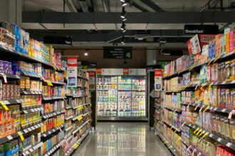 Συσκευασίες καφέ σε ράφι σούπερ μάρκετ με ετικέτα χαμηλής τιμής σε πρώτο πλάνο, θολό φόντο διαδρόμου καταστήματος