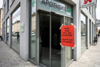 Κλειστή γυάλινη πόρτα γερμανικού φαρμακείου με αναρτημένη κόκκινη ανακοίνωση απεργίας