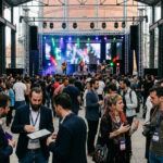 Eine gut beleuchtete Konzertbühne und diskutierendes Fachpublikum während der Athens Music Week