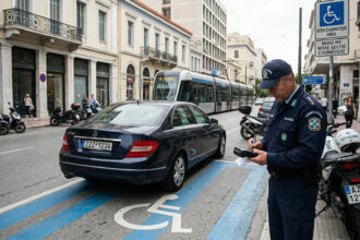 Ein falsch geparktes Auto auf einem Behindertenparkplatz in Griechenland, während ein Polizist einen Strafzettel schreibt
