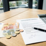 Euro-Banknoten und Münzen liegen neben einem Taschenrechner und einem Arbeitsvertrag auf einem Schreibtisch.