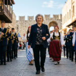 Eine ältere Frau marschiert stolz in traditioneller oder schulischer Kleidung bei einer sonnigen Parade auf Rhodos