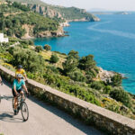 Radfahrer auf einer Küstenstraße in Griechenland bei sonnigem Wetter im Frühling.