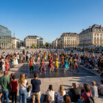 Eine Menschenmenge genießt eine kulturelle Aufführung auf einem sonnigen Platz in Athen