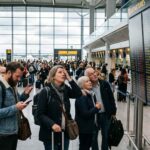 Ταξιδιώτες παρακολουθούν με αγωνία τις οθόνες πληροφοριών πτήσεων σε ένα σύγχρονο αεροδρόμιο της Ευρώπης