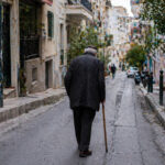 Eine ältere Person geht durch eine städtische Straße in Griechenland, symbolisch für die sinkende Kaufkraft und hohe Wohnkosten.