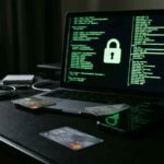 Σκοτεινή οθόνη υπολογιστή με πράσινους κωδικούς και ψηφιακά νομίσματα δίπλα σε πιστωτικές κάρτες