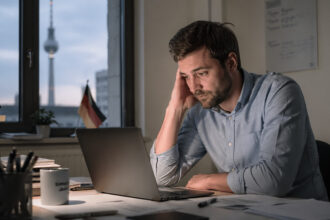 Ένας υπάλληλος γραφείου κάθεται προβληματισμένος μπροστά από τον υπολογιστή του αργά το απόγευμα