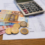 Euroscheine und Münzen liegen auf einem Tisch neben Formularen und einem Taschenrechner
