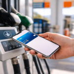 Eine Person hält ein Smartphone an ein Zahlungsterminal an einer Tankstelle in Griechenland.