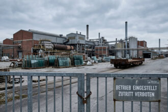 Εξωτερική όψη μεγάλου βιομηχανικού εργοστασίου με κλειστές πύλες και συννεφιασμένο ουρανό