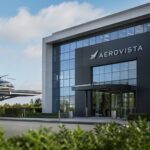 Zivile und militärische Hubschrauber auf einem Flugfeld vor einem modernen Bürogebäude.