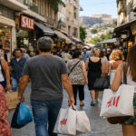 Kunden gehen an einem sonnigen Tag in einer griechischen Einkaufsstraße mit geöffneten Geschäften spazieren