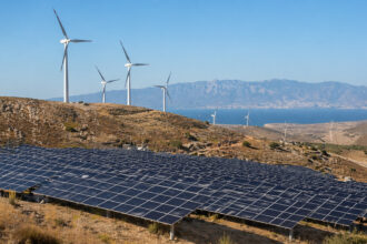 Moderne Windkraftanlagen und großflächige Solarparks in der sonnigen griechischen Landschaft.