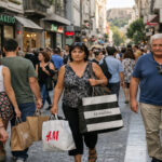 Menschen gehen in einer Einkaufsstraße in Athen mit Einkaufstüten spazieren, Tageslicht.
