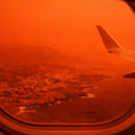 Ein Passagierflugzeug fliegt durch einen rot und orange gefärbten Himmel voller Saharastaub über Kreta.