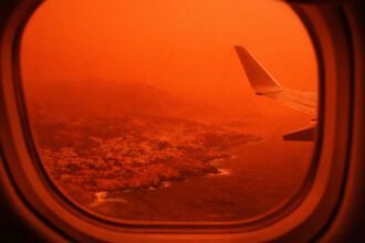 Ein Passagierflugzeug fliegt durch einen rot und orange gefärbten Himmel voller Saharastaub über Kreta.