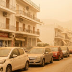 Eine dichte Wolke aus Saharastaub trübt den Himmel über einer griechischen Stadt, während Autos im diffusen Licht fahren.