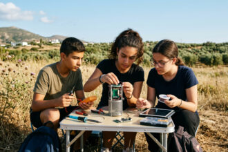 Griechische Schüler bereiten auf einem Feld einen kleinen Satelliten für den Start vor