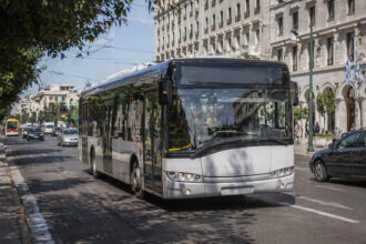 Ein moderner städtischer Bus fährt durch eine griechische Metropole, unmarkiert, bereit für ein neues Design.