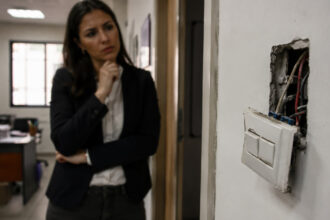 Eine Frau in Bürokleidung betrachtet besorgt einen defekten Lichtschalter an der Wand