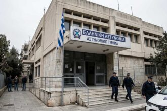 Δικαστικό μέγαρο με φόντο την ελληνική σημαία κατά τη μεταγωγή συλληφθέντα