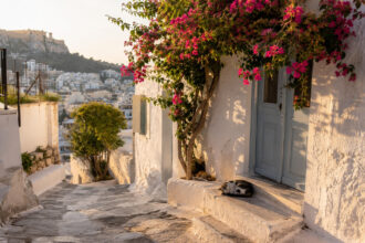 Eine malerische, sonnendurchflutete Gasse im Viertel Anafiotika in Athen unter strahlend blauem Himmel.