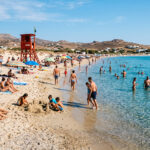 Ein roter Rettungsschwimmerturm an einem gut besuchten Sandstrand in Griechenland bei sonnigem Wetter