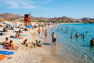 Ein roter Rettungsschwimmerturm an einem gut besuchten Sandstrand in Griechenland bei sonnigem Wetter