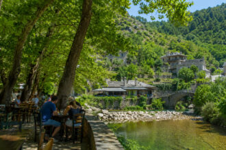 Ein traditionelles griechisches Bergdorf aus Stein umgeben von dichten grünen Wäldern und einem Fluss