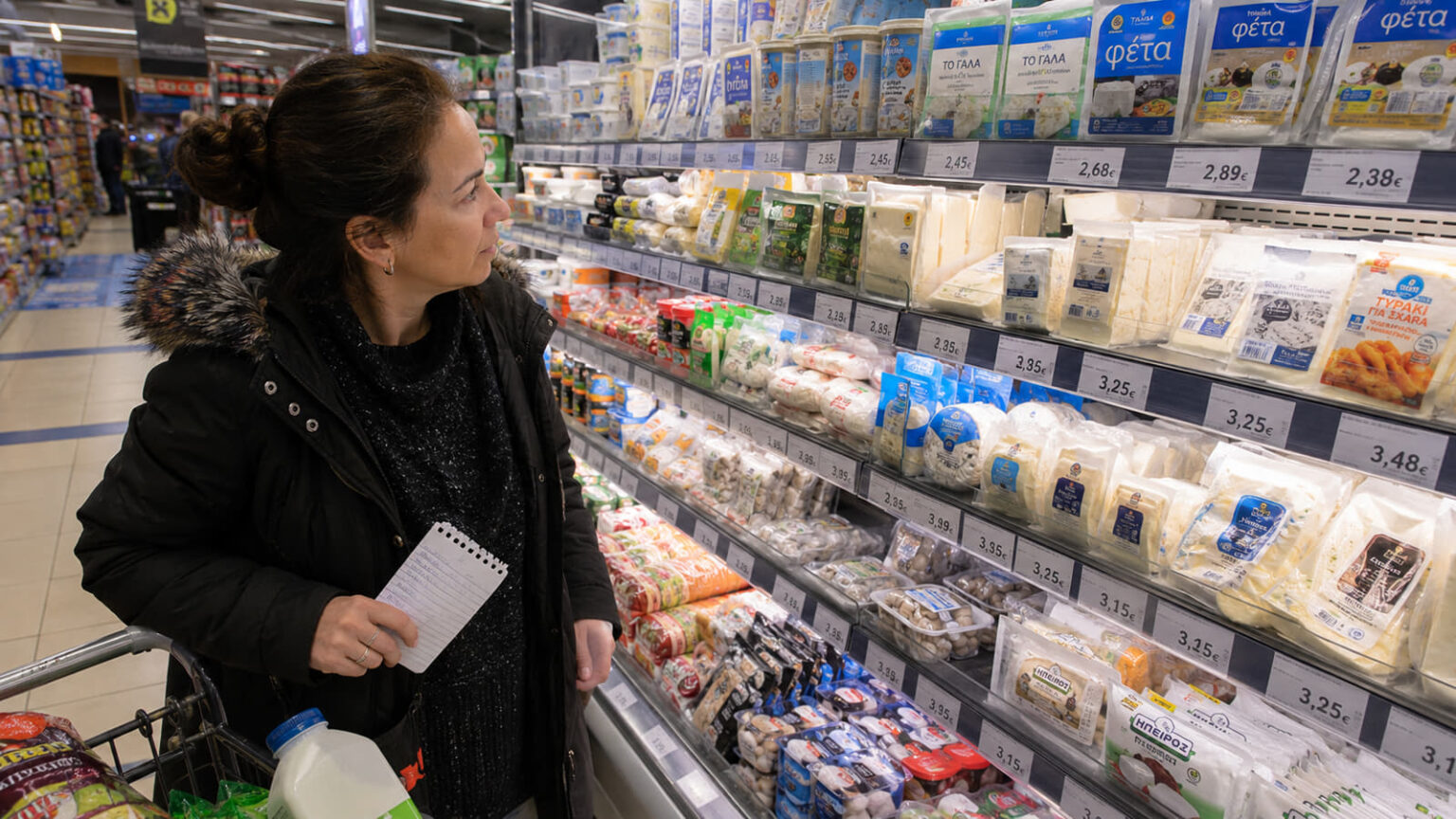 Ein Einkaufswagen in einem griechischen Supermarkt mit verschiedenen Markenprodukten und Preisschildern.