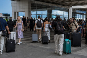 Reisende mit Gepäckstücken an einem hellen internationalen Flughafen in Griechenland während der Urlaubssaison
