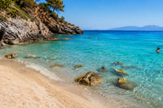 Menschen entspannen am Strand mit kristallklarem, türkisfarbenem Wasser in Griechenland