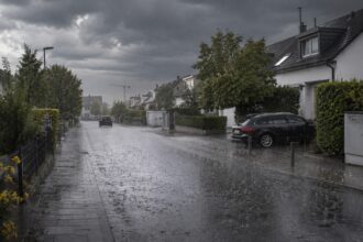 Βαριά σύννεφα και βροχή πάνω από γερμανική πόλη, με βρεγμένο οδόστρωμα και μειωμένη ορατότητα.