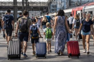 Οικογένειες με αποσκευές και μαθητές περπατούν σε κεντρικό σιδηροδρομικό σταθμό της Γερμανίας κατά την περίοδο των θερινών διακοπών.