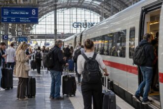 Επιβάτες περιμένουν στην αποβάθρα μεγάλου σιδηροδρομικού σταθμού στη Γερμανία δίπλα σε ένα σύγχρονο τρένο