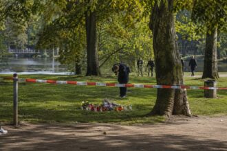 Αστυνομικοί στο Wuppermann-Park στο Leverkusen ερευνούν το σημείο της δολοφονίας του 20χρονου, δίπλα σε λουλούδια και κεριά.