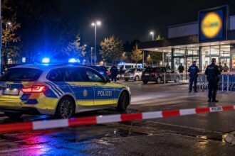 Αστυνομικό όχημα με αναμμένους φάρους έξω από χώρο στάθμευσης σούπερ μάρκετ στη Γερμανία κατά τη διάρκεια της νύχτας.
