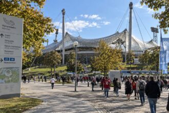 Εξωτερική άποψη του σταδίου Olympiastadion στο Μόναχο με κόσμο να περπατά στον περιβάλλοντα χώρο