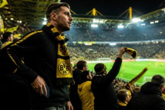 Οπαδός της Borussia Dortmund με κιτρινόμαυρο κασκόλ αφήνει το κινητό του στην άκρη στις εξέδρες γηπέδου